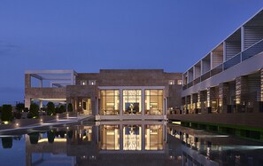 A modern hotel with a reflective pool, large windows, and a well-lit lobby area. - Pelagos Suites Hotel & Spa (Kos)