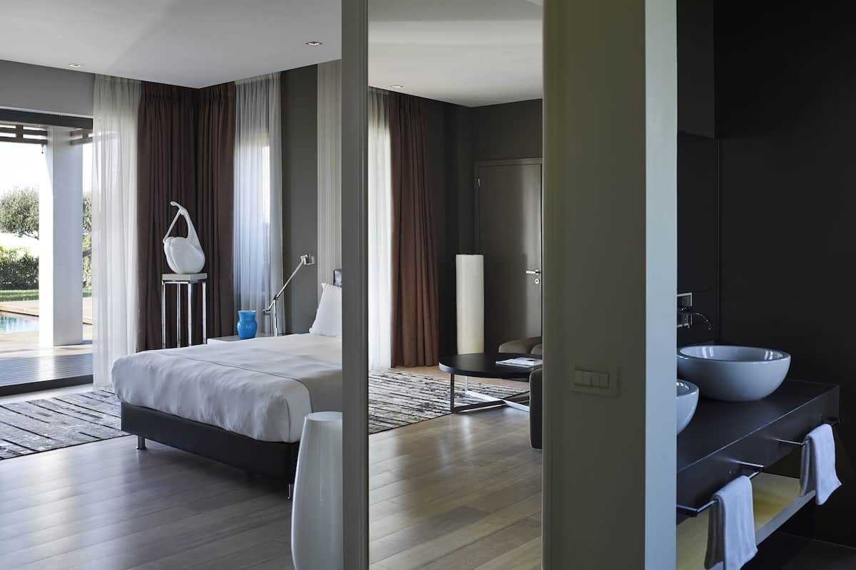 A modern bedroom with a large bed, a bedside table, a nightstand, and a bathroom with a large sink and mirror.