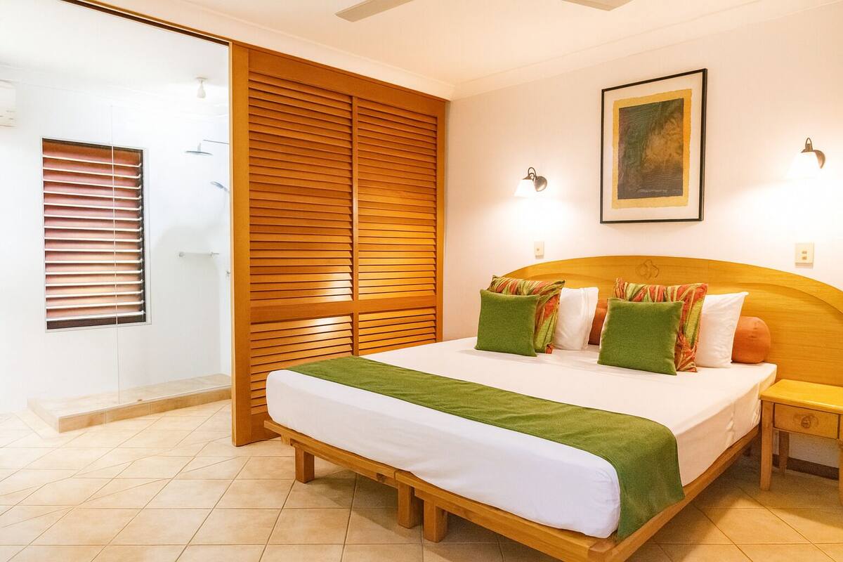 A bedroom with a wooden headboard, a bed with green and white bedding, a nightstand, and a painting on the wall.