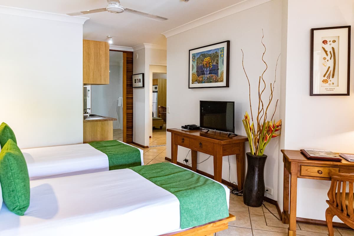 A hotel room with two beds, a TV, a desk, and a dining area.