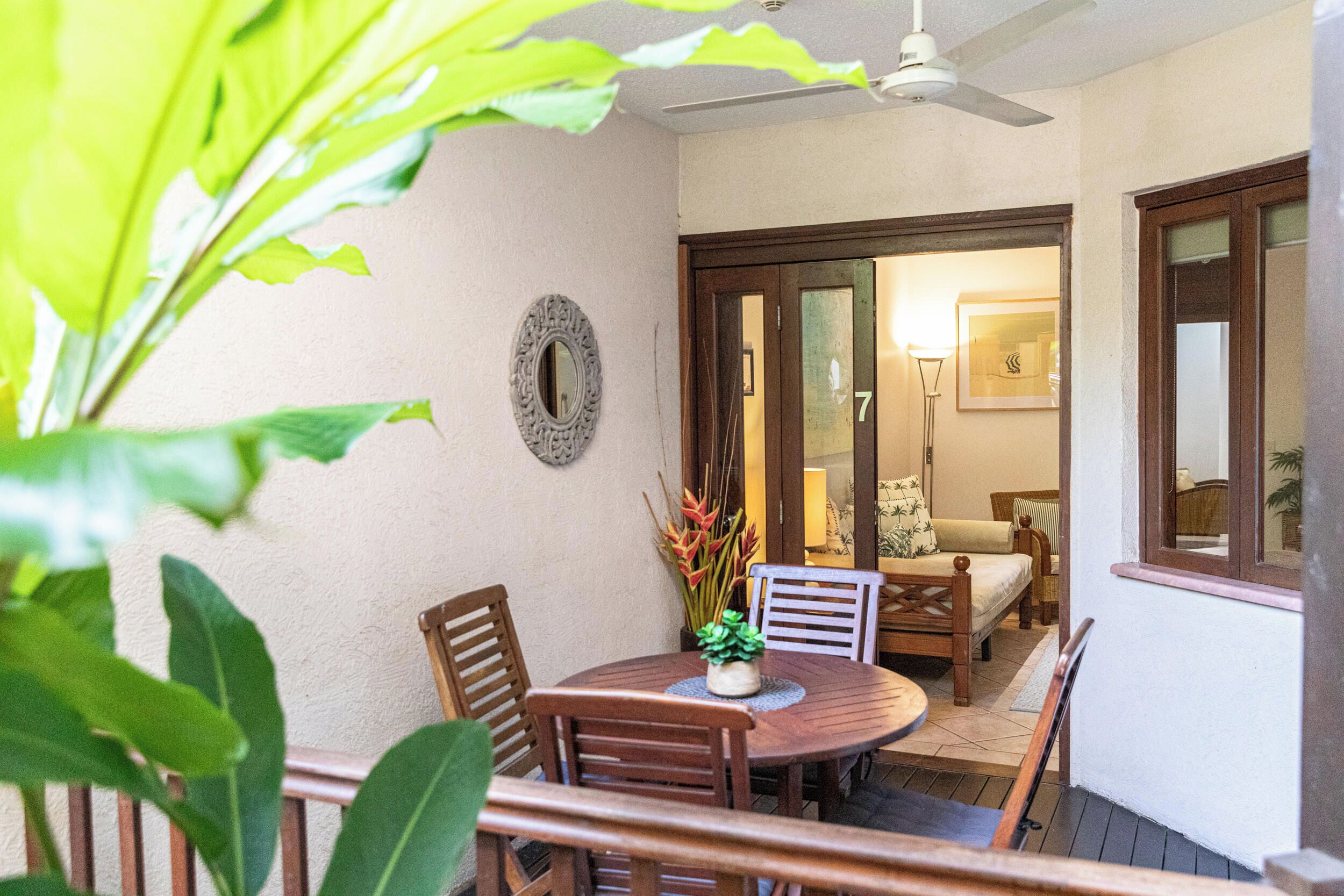 A patio with a round wooden table and chairs, a potted plant, and a ceiling fan.
