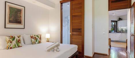 A bedroom with a bed, pillows, a bedside lamp, a framed artwork, and a wooden door leading to a bathroom.