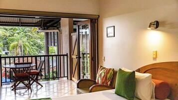 A hotel room with a bed, a sofa, a table with chairs, and a balcony with a view of palm trees.