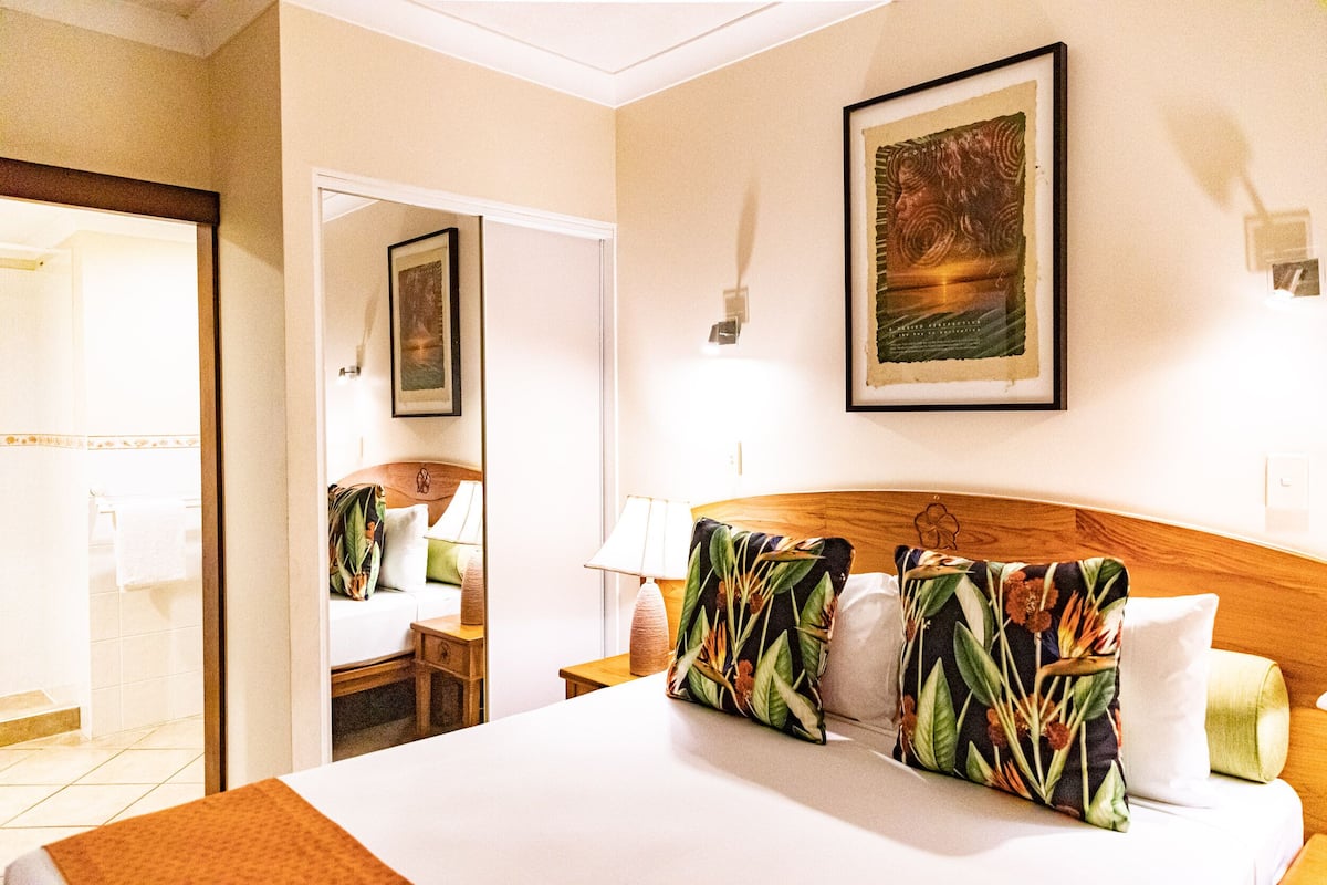 A hotel room with a bed, a nightstand, a mirror, and a framed picture on the wall.