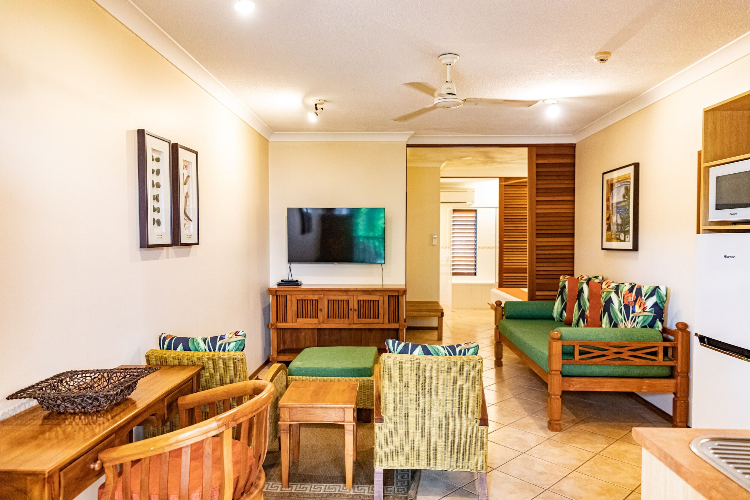 A living room with a television, wicker furniture, and a ceiling fan.