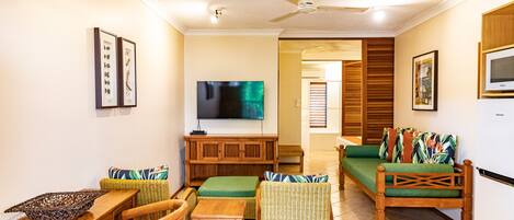 A living room with a television, wicker furniture, and a ceiling fan.