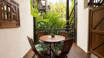 A wooden deck with a round table and chairs, surrounded by lush tropical plants.