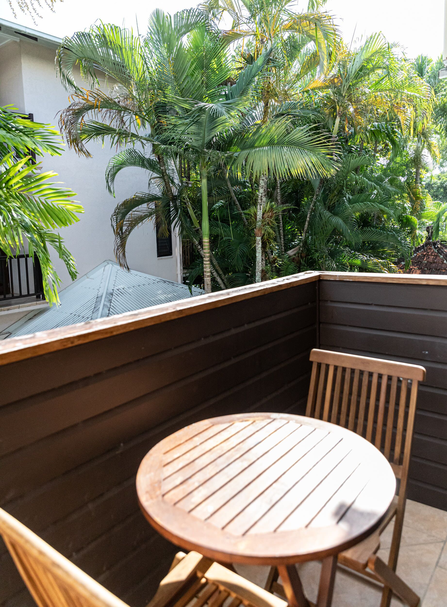 A wooden table and chairs in a corner with a view of a lush garden and palm trees.