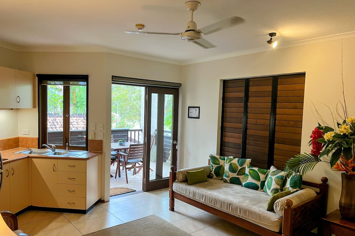 A modern kitchen with a dining area, a sofa with patterned cushions, and a ceiling fan.
