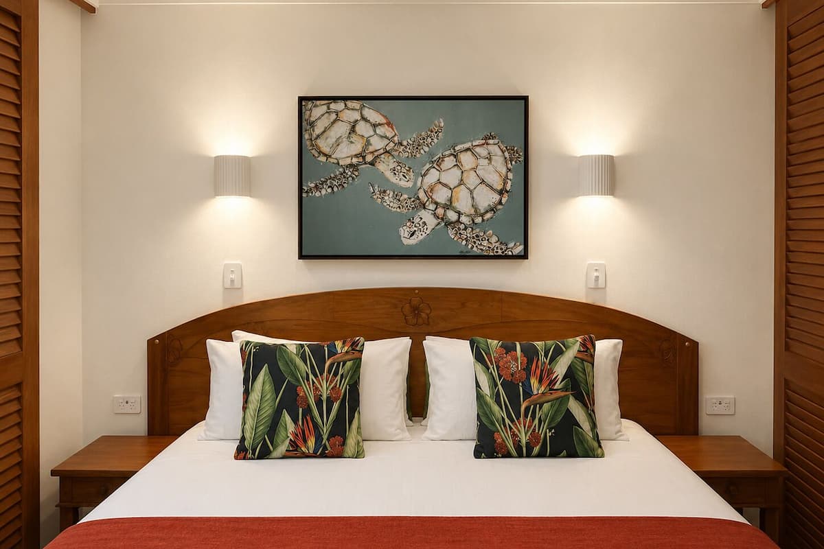 A hotel room with a large bed, two nightstands, a wooden headboard, a framed artwork of sea turtles, and two wall-mounted lamps.