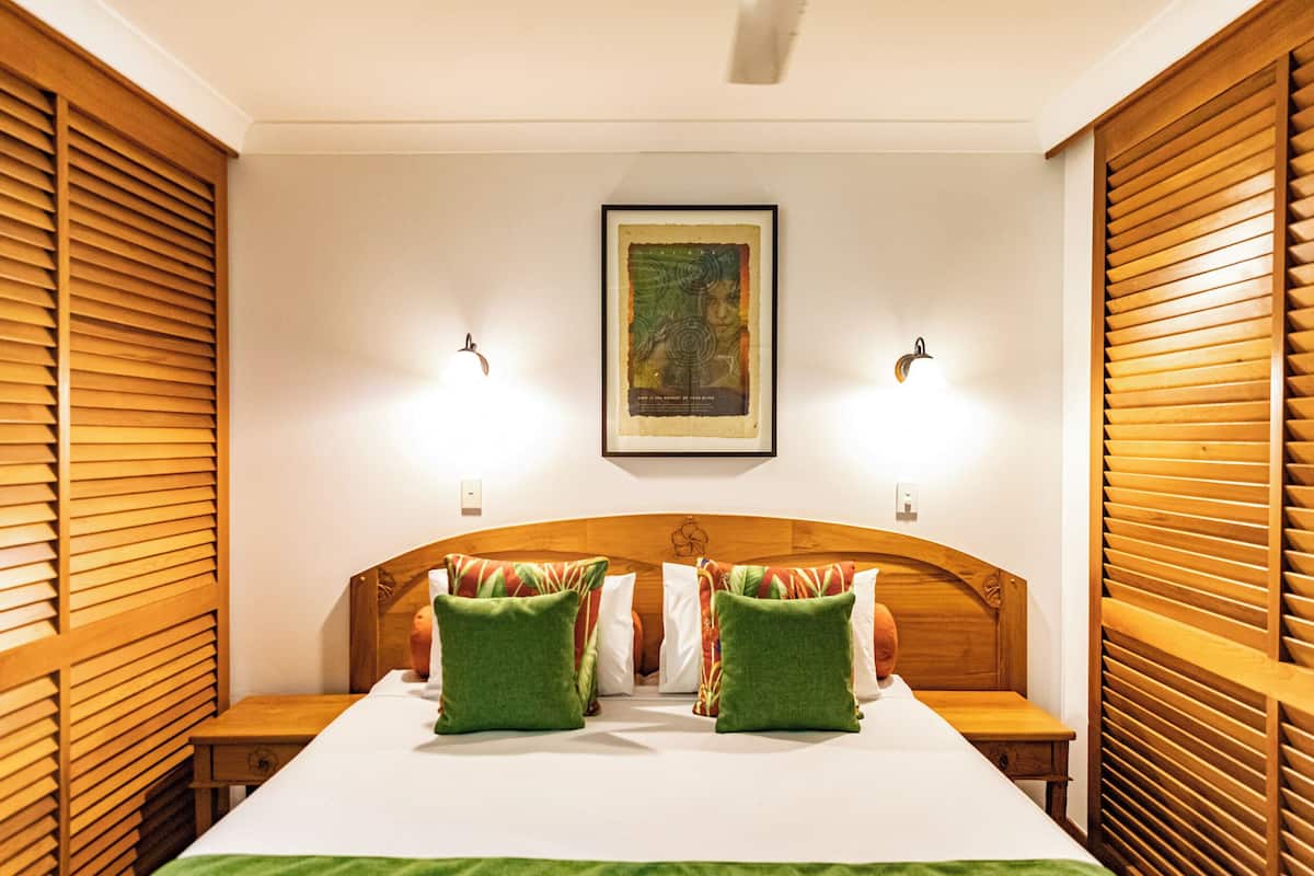A hotel room with a wooden headboard, two bedside tables, a bed with green and white bedding, and a framed picture on the wall.