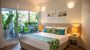 Habitación de hotel con una cama grande, dos lámparas de noche, vistas a un patio con sillas y plantas, y una obra de arte en la pared.