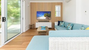 Un salón moderno con televisor, sofá y vistas a una playa a través de una ventana.