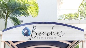 Una entrada con temática playera, con una palmera, un cartel que dice "Beaches Port Douglas" y una zona de recepción.
