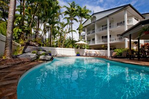 Una piscina con cerco blanco, palmeras y un edificio con balcones.