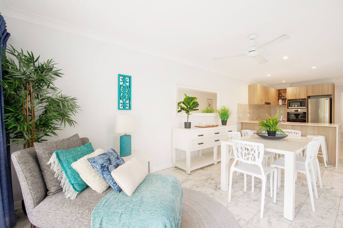 Una sala de estar moderna con un sofá, una mesa de comedor y sillas. Hay una zona de cocina con un refrigerador y microondas.