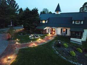 Uma casa de dois andares com telhado escuro, chaminé visível e entrada bem iluminada.