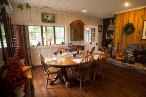 Uma sala de jantar com uma mesa de madeira posta para seis pessoas, rodeada por cadeiras de madeira.