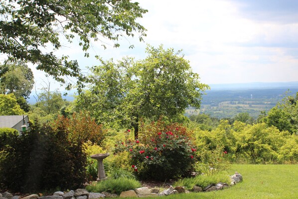A garden with a stone birdbath, lush greenery, and a view of distant hills. - Antietam Overlook Farm (Keedysville)