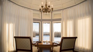 A room with two chairs facing a large window, a chandelier, and a table with candles. - Antietam Overlook Farm (Keedysville)