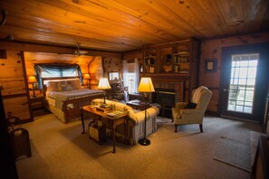 Interior acolhedor de uma cabana de madeira com cama, sofá, poltrona, escrivaninha e lareira.