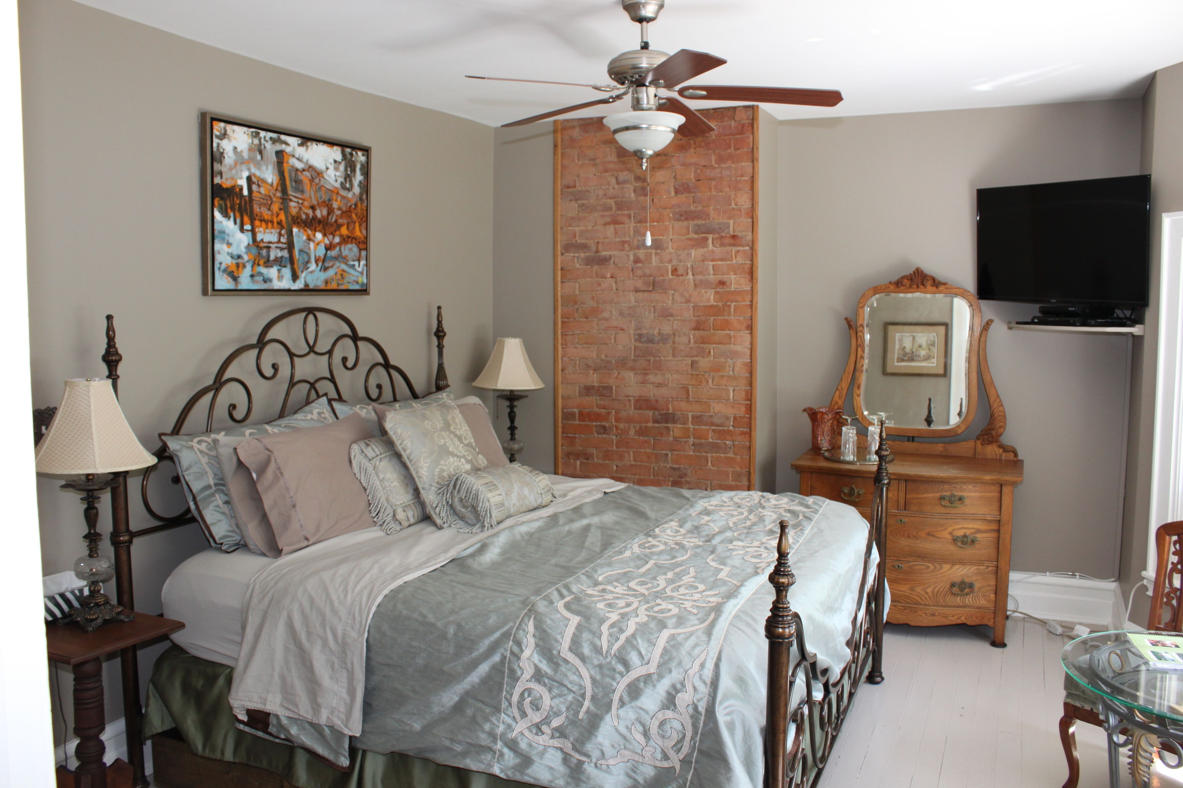 A bedroom with a bed, a dresser, a mirror, a television, and a ceiling fan.