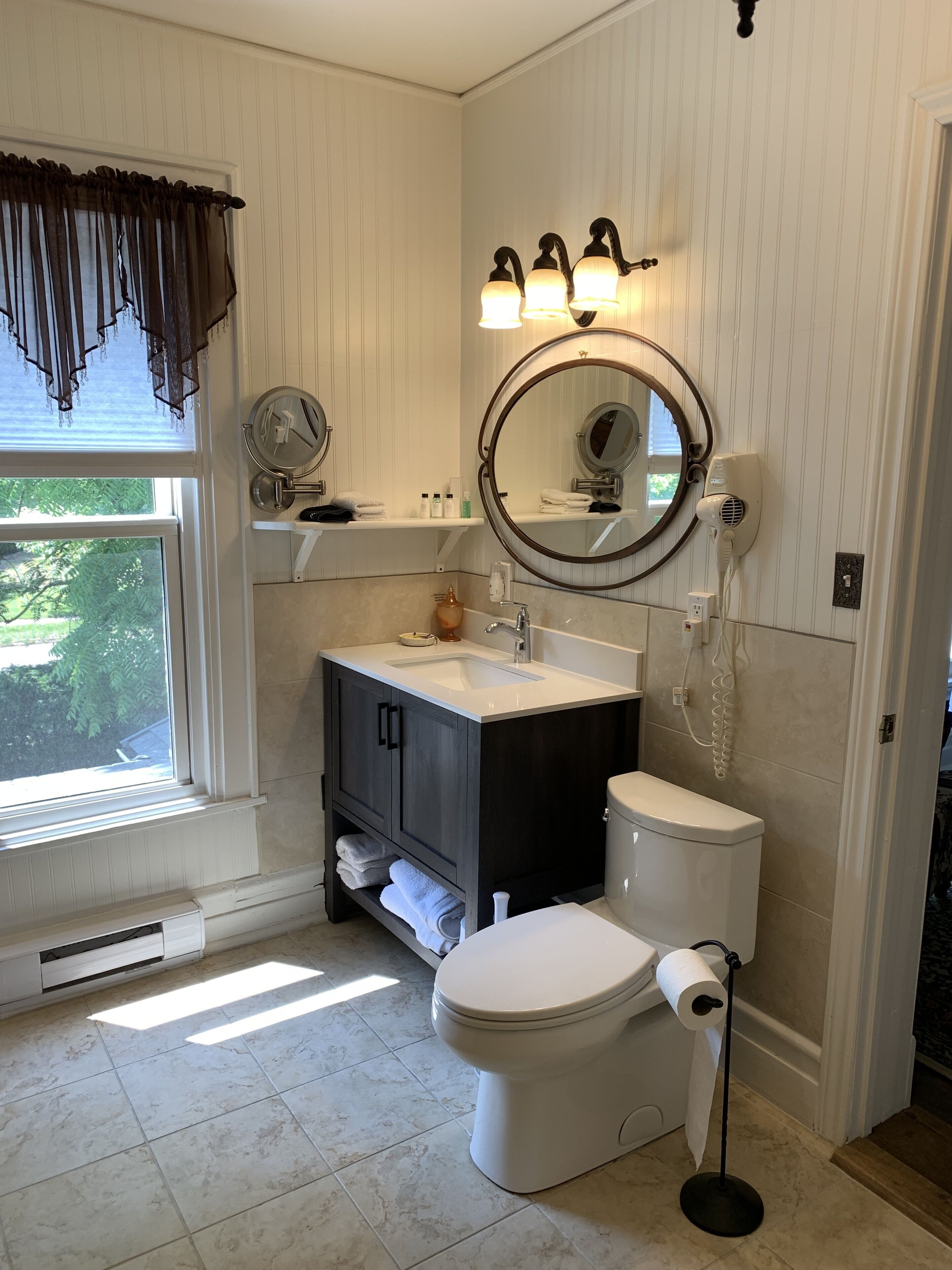 A bathroom with a toilet, sink, vanity, and a large mirror.
