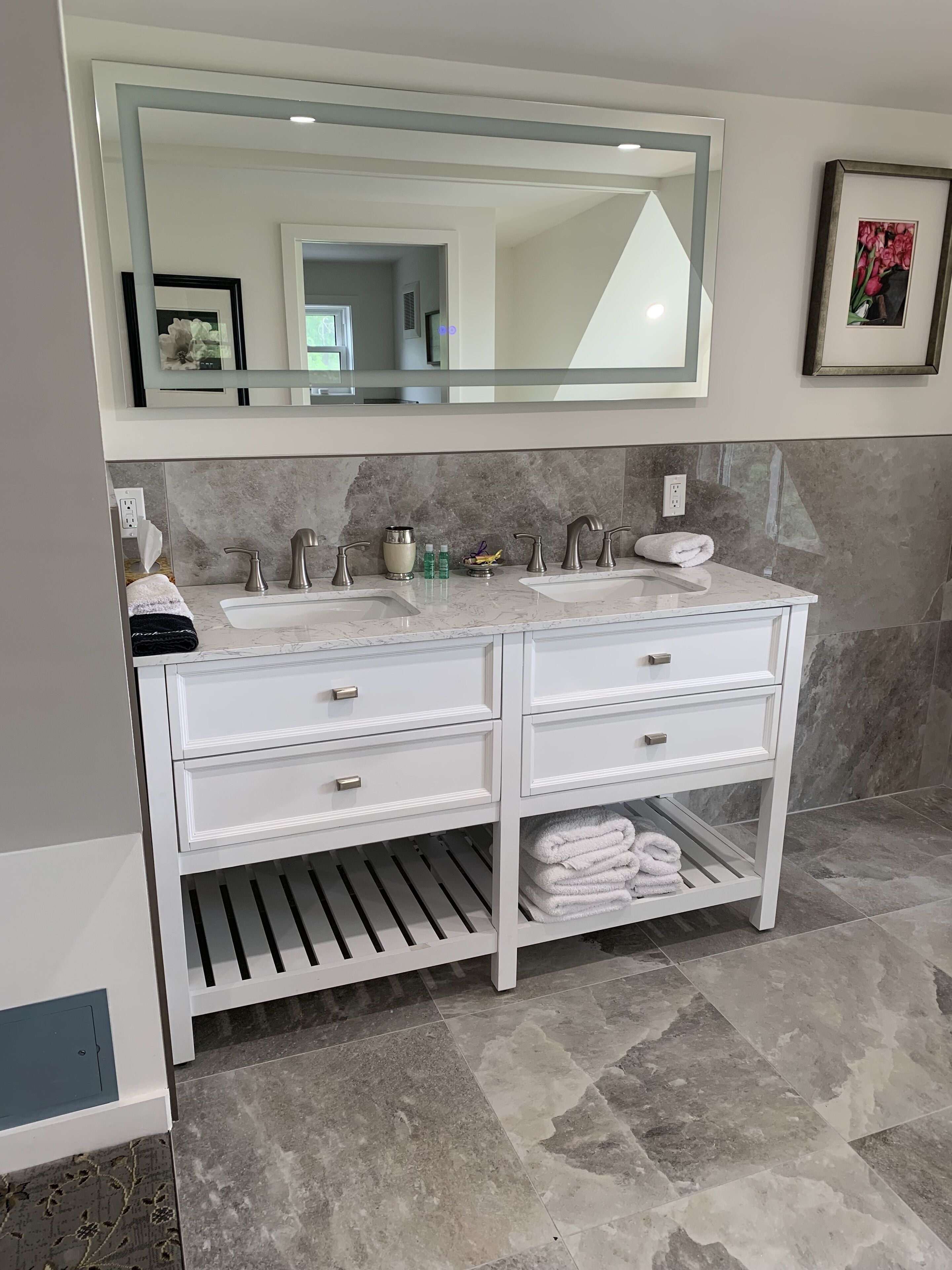 Une salle de bain avec un meuble-lavabo blanc, deux vasques, un grand miroir et un porte-serviettes.