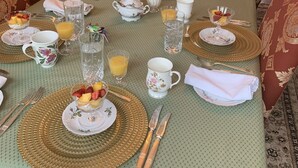 A formal dining room with a long table set for breakfast, featuring gold-rimmed plates, white teacups, and a variety of breakfast items. - Green Oaks Bed and Breakfast (Niagara-on-the-Lake)