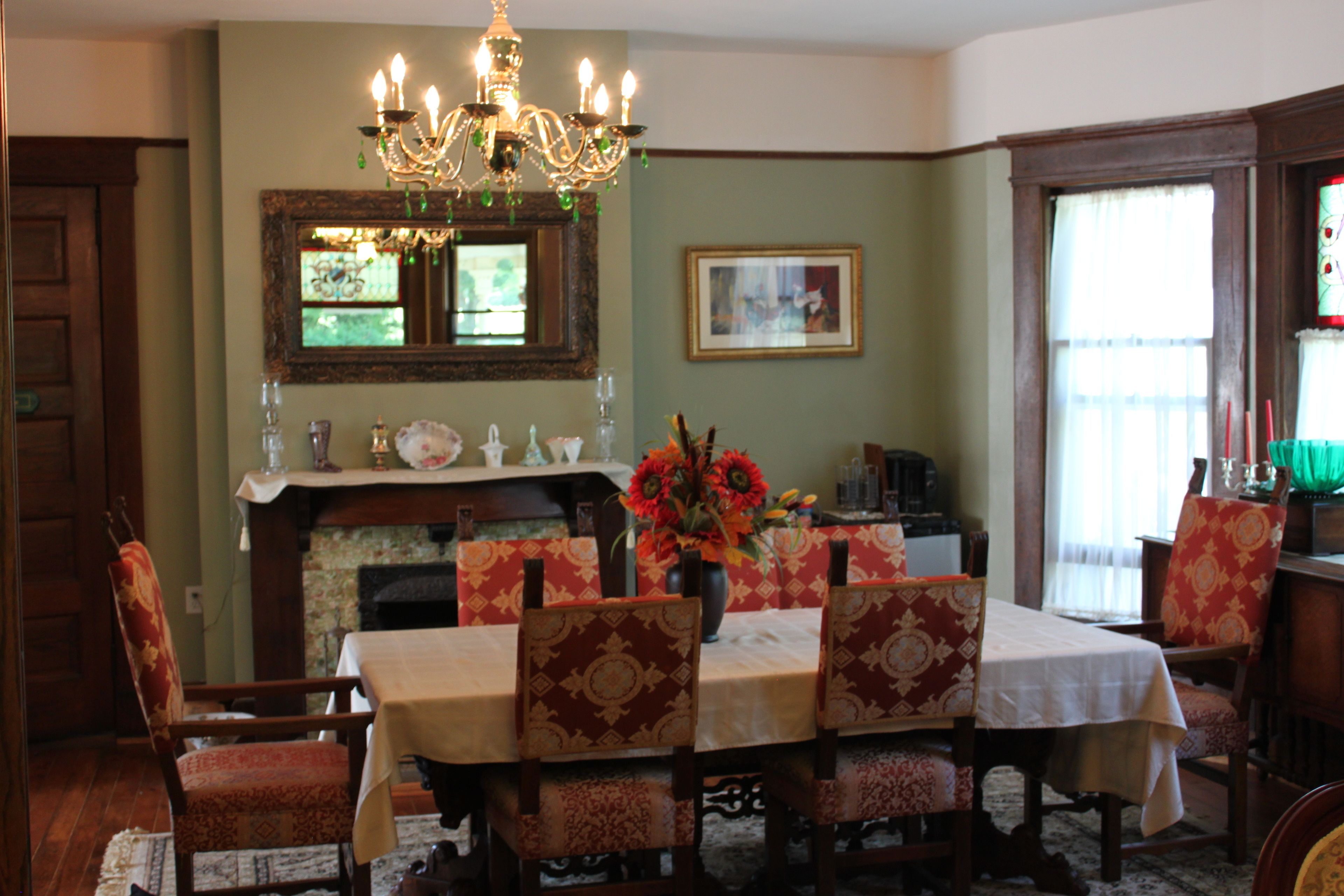 Uma sala de jantar com um candelabro, uma lareira e uma mesa posta para quatro pessoas.