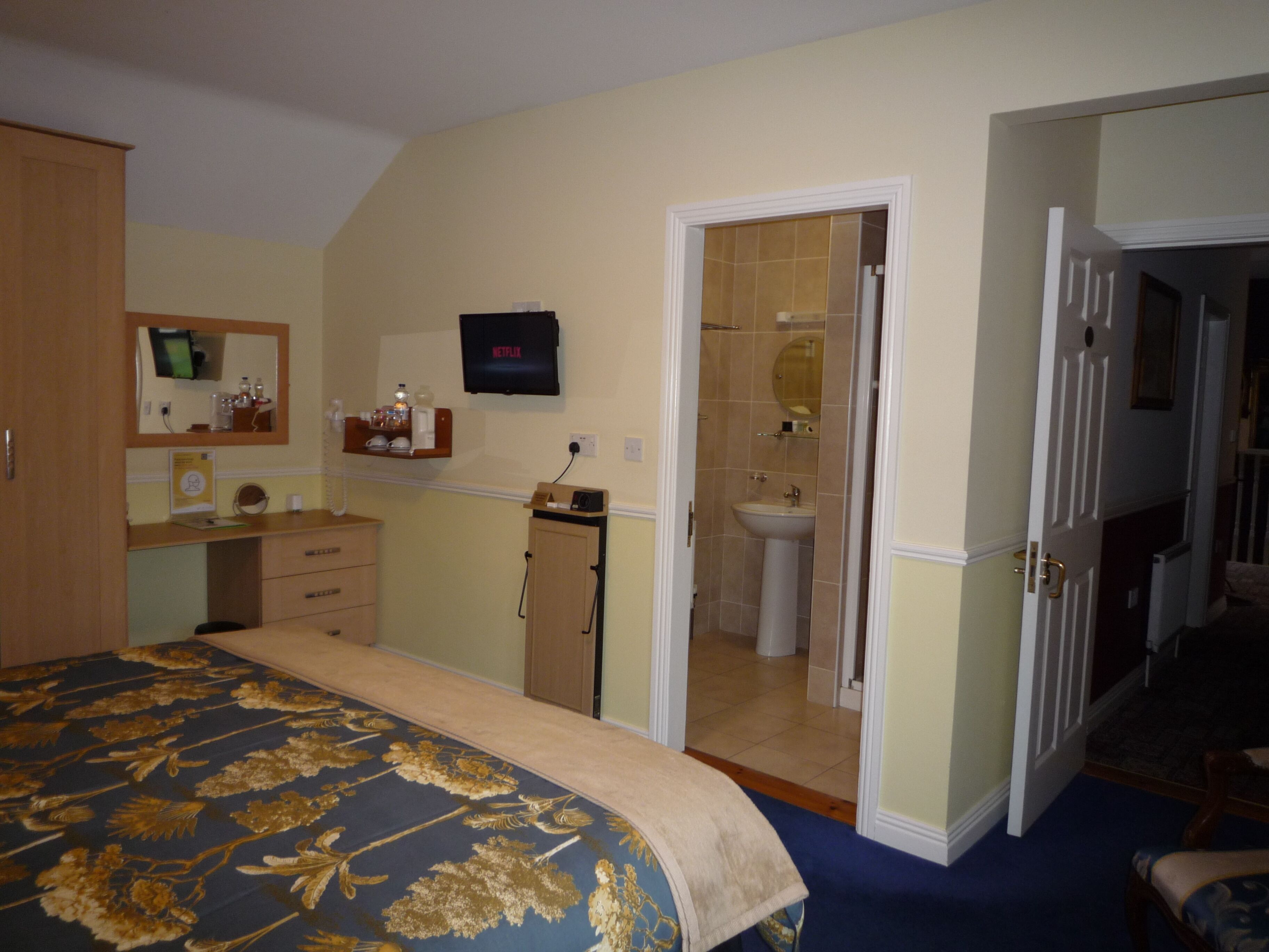 Habitación con cama, cómoda, televisor y baño visible a través de una puerta abierta.
