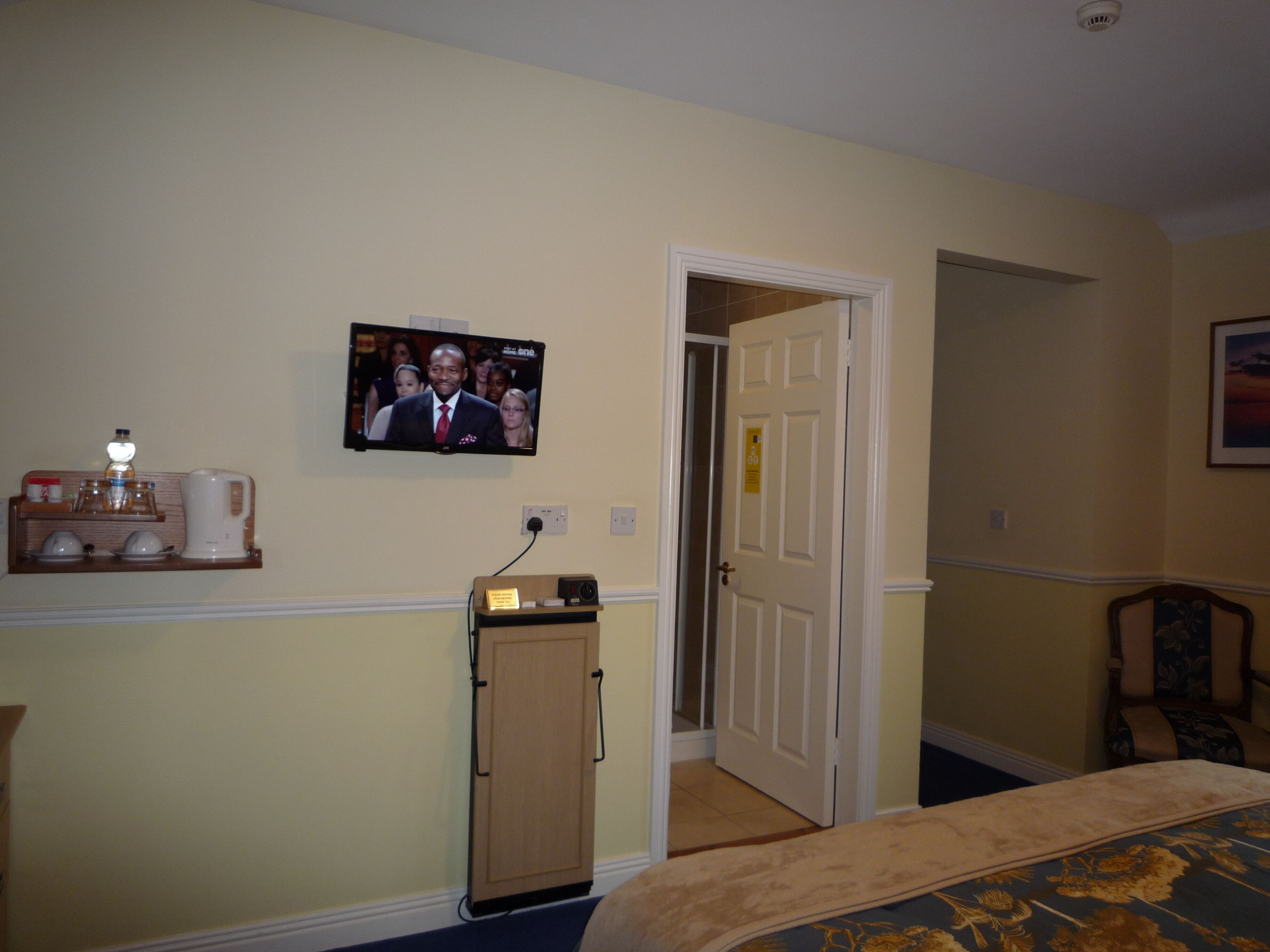 Une chambre d’hôtel comprenant un lit, un téléviseur fixé au mur, une petite armoire et une porte donnant sur une autre pièce.