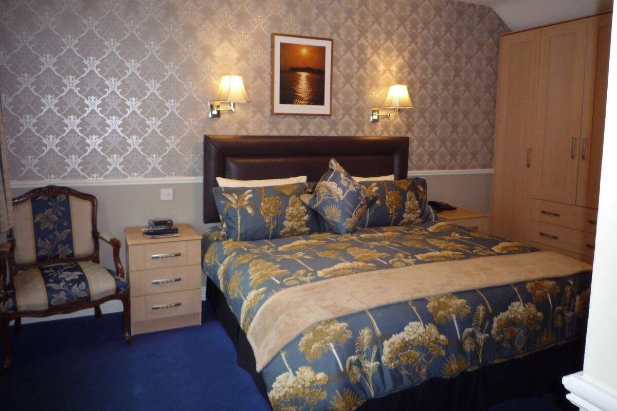 Une chambre à coucher avec un lit, deux lampes de chevet, une chaise, une commode et un tableau encadré au mur.