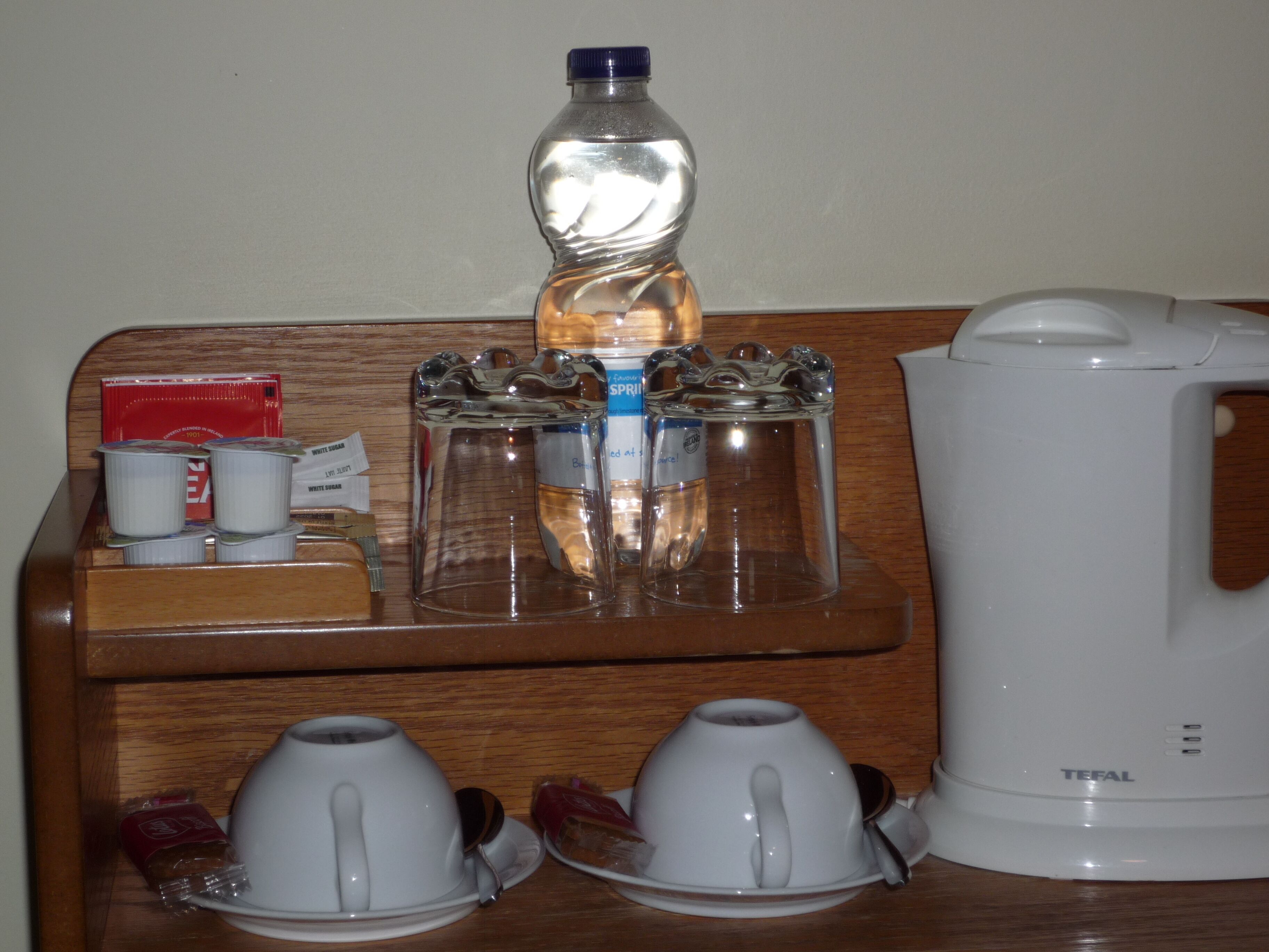 Una mesa de madera con una botella de agua, una cafetera y dos tazas blancas.