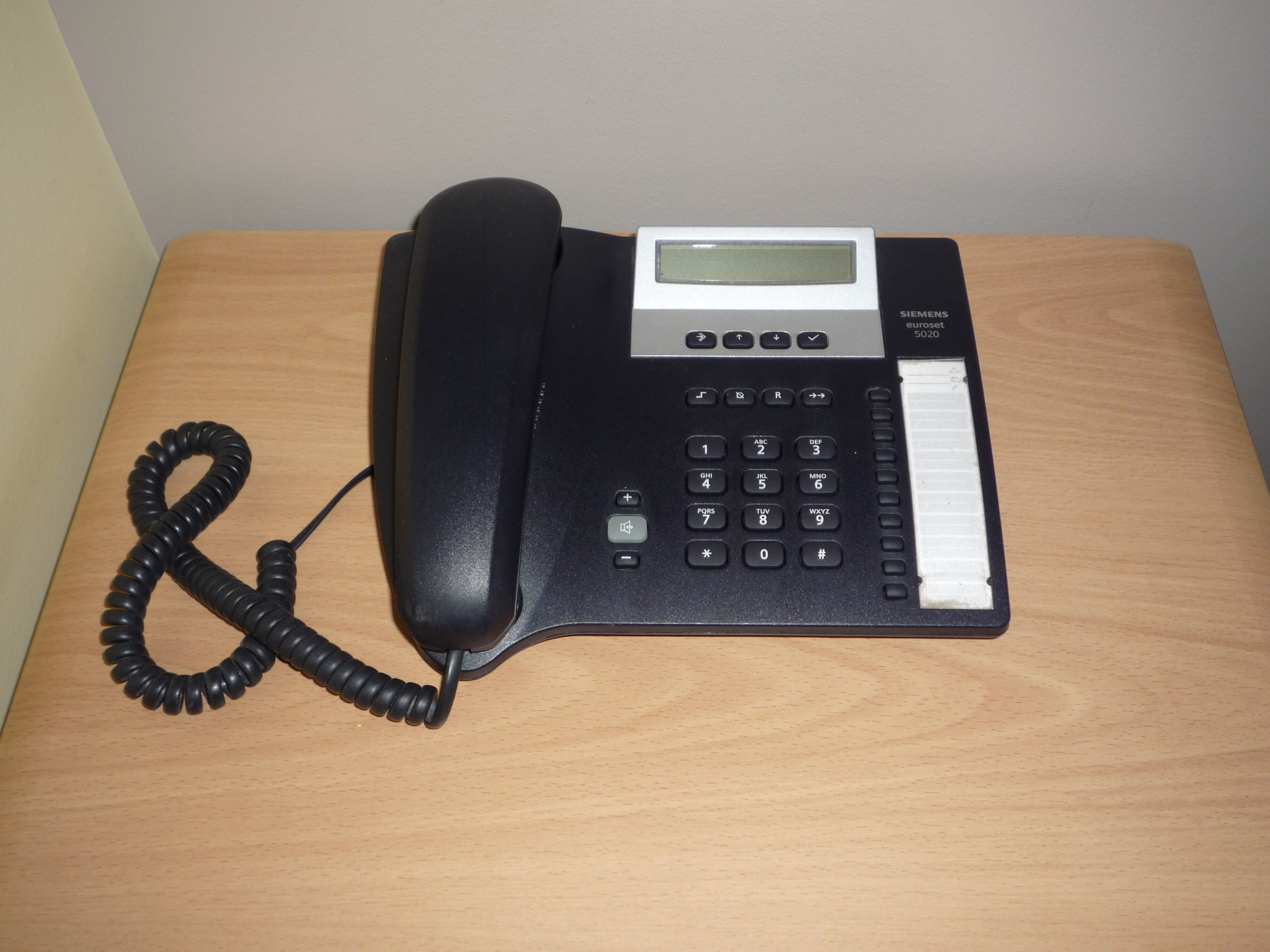 Ein schwarzes Telefon mit Tastatur und kleinem Bildschirm auf einem Holztisch.