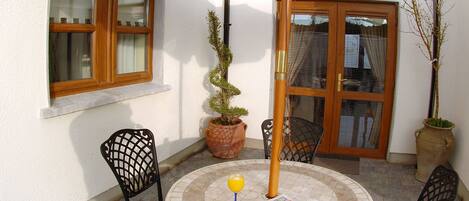 A patio with a round table, four chairs, a large umbrella, and potted plants.
