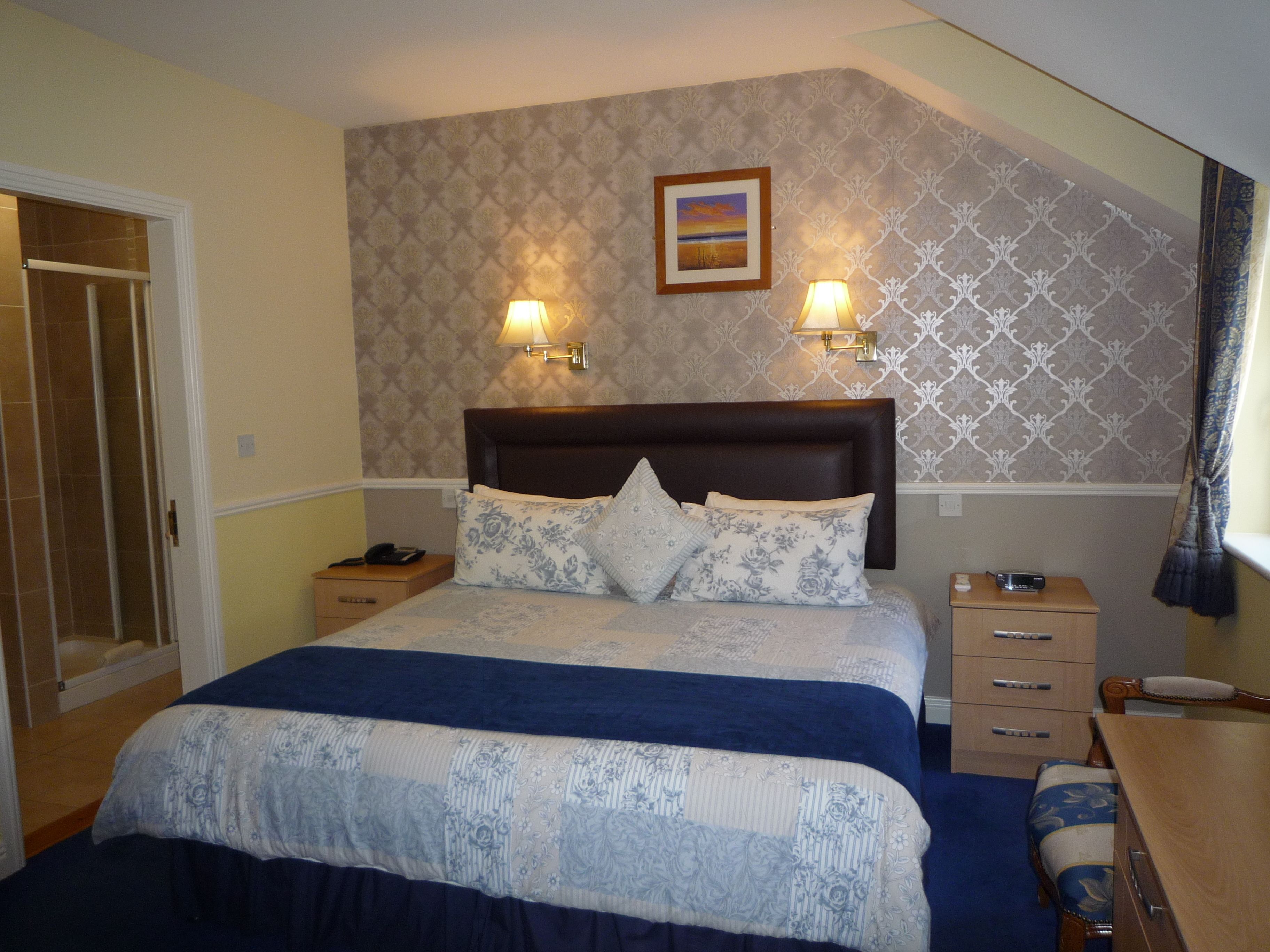 Quarto com uma cama grande, duas luminárias de cabeceira, uma mesinha de cabeceira, um aparador de madeira e uma moldura com um quadro na parede.