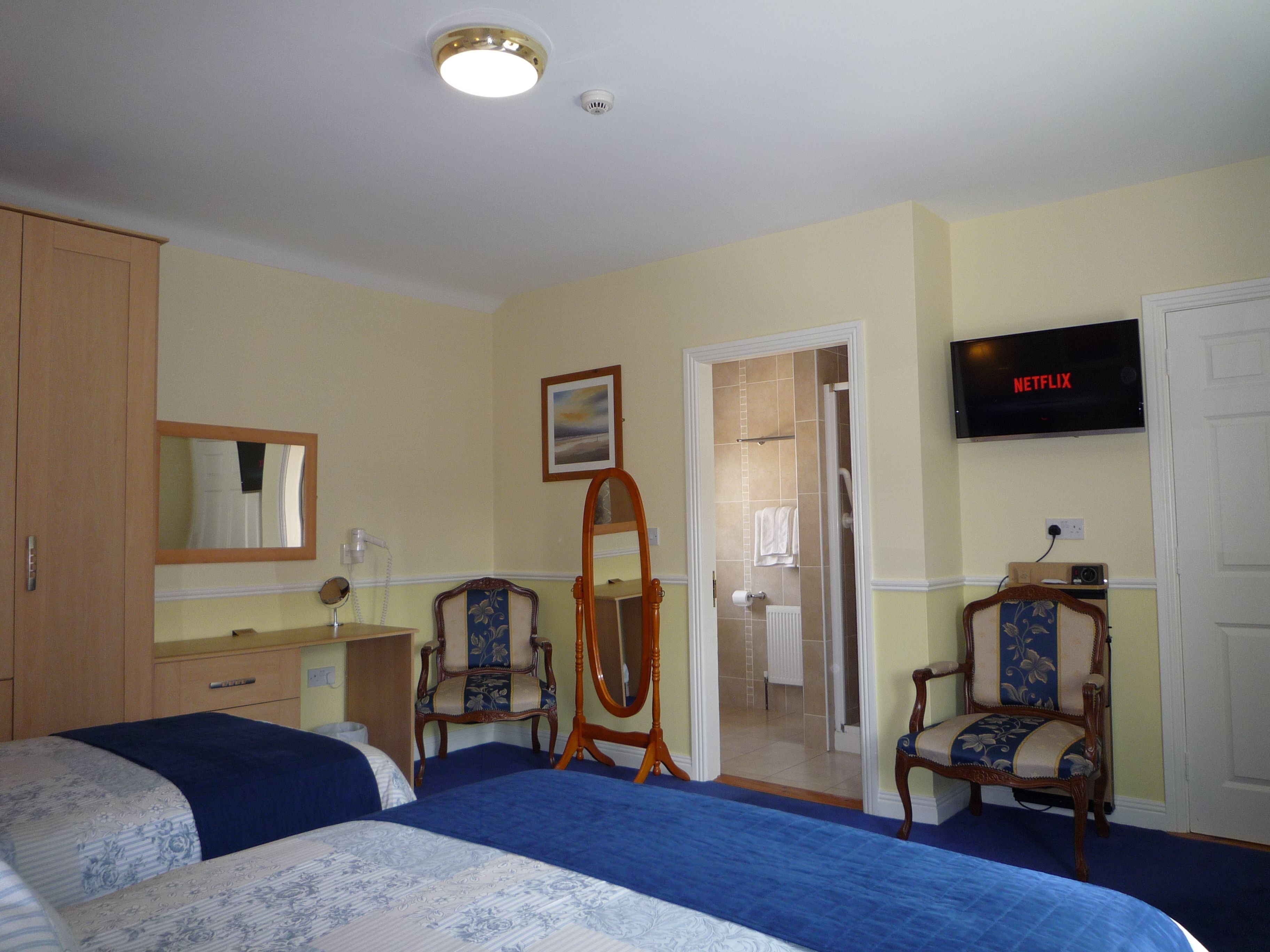 A hotel room with two beds, a television, a mirror, a dresser, and a door leading to a bathroom.