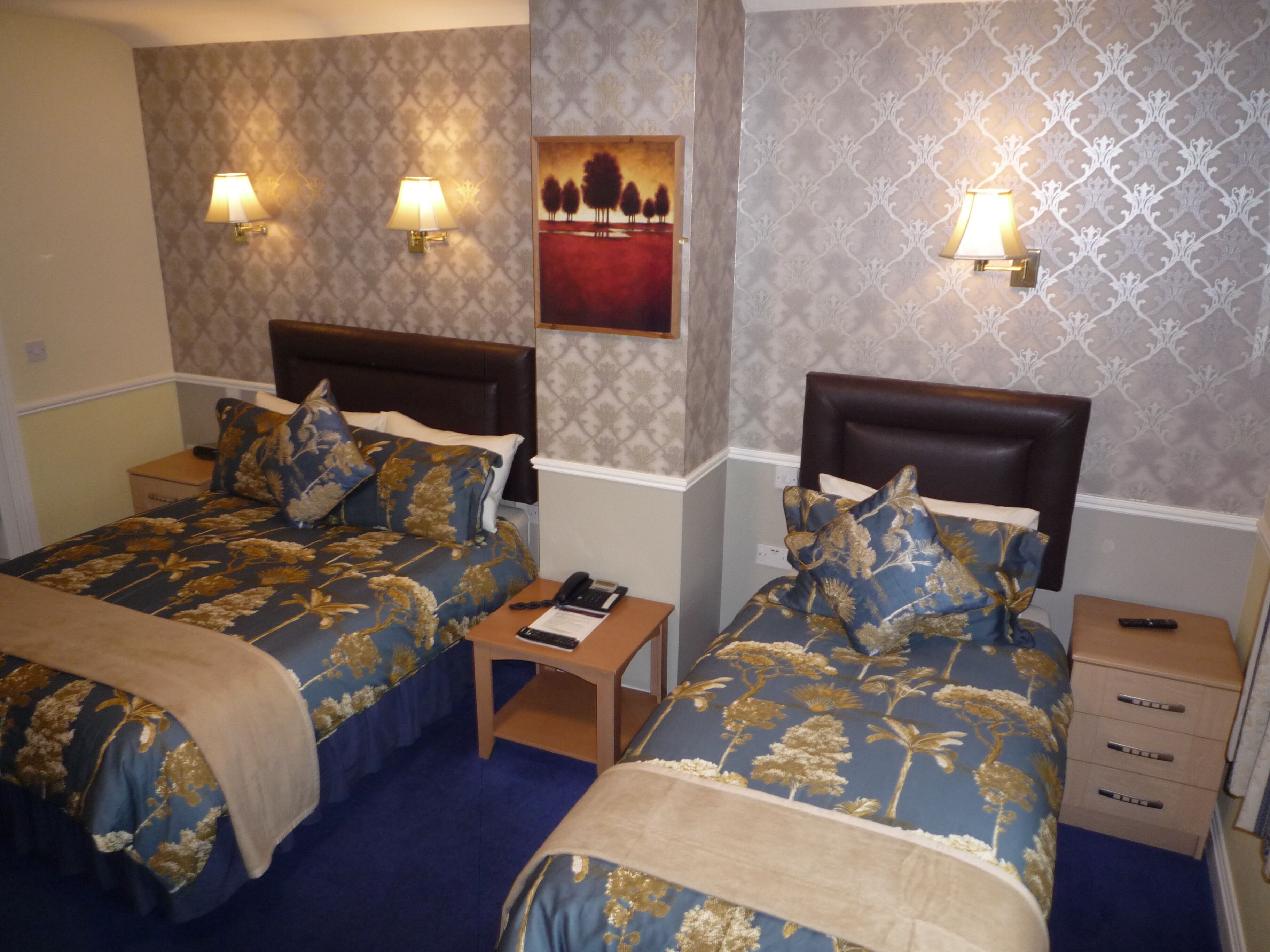 A hotel room with two beds, each with a headboard, a nightstand, a lamp, and a painting on the wall.