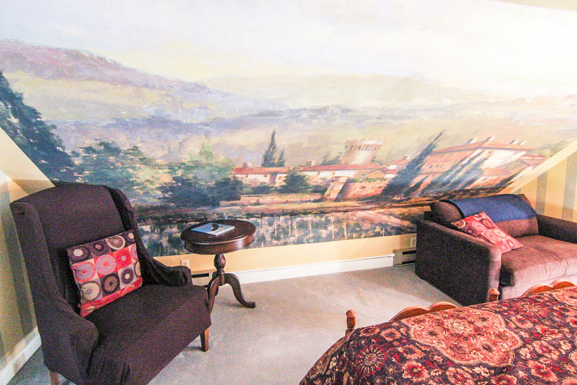 A room with a view of a landscape through a large window, featuring a chair, a sofa, and a small table.