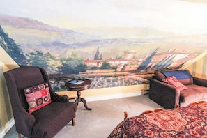 Une pièce offrant une vue sur un paysage grâce à une grande fenêtre, et comprenant un fauteuil, un canapé et une petite table.