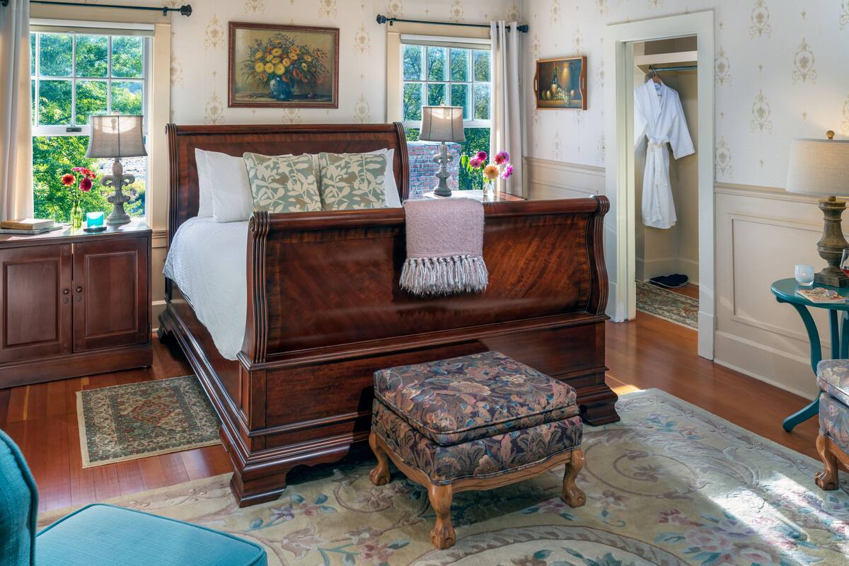 Quarto tradicional com uma cama de dossel de madeira, um banco harmonioso e vista do exterior por grandes janelas.