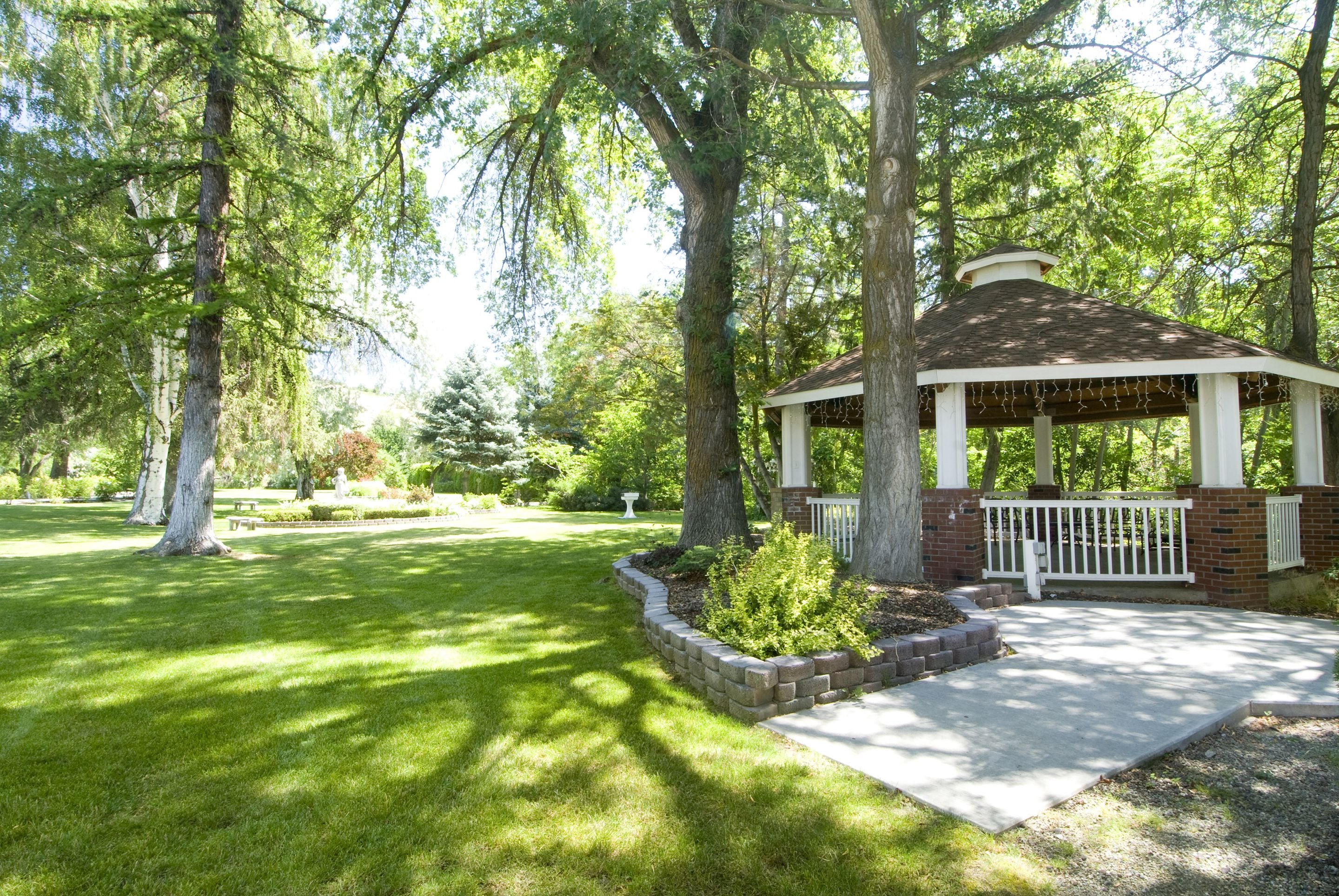 A gazebo with a brick base and white railings, surrounded by a well-maintained lawn and mature trees.