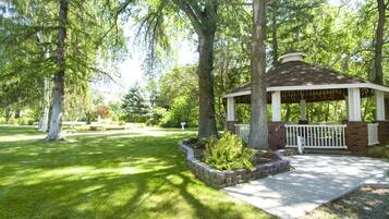 A gazebo with a brick base and white railings, surrounded by a well-maintained lawn and mature trees.