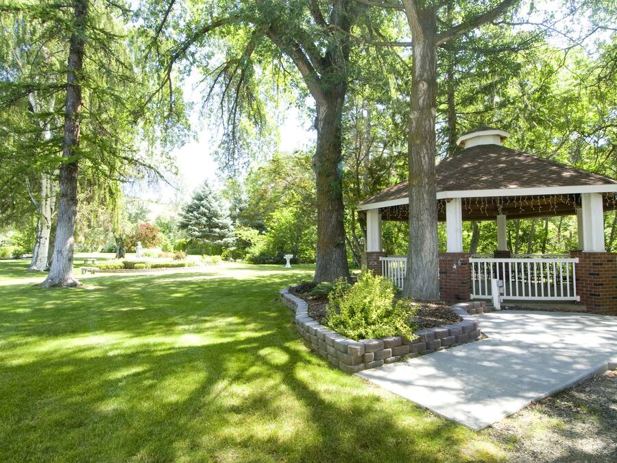A gazebo with a brick base and white railings, surrounded by a well-maintained lawn and mature trees.