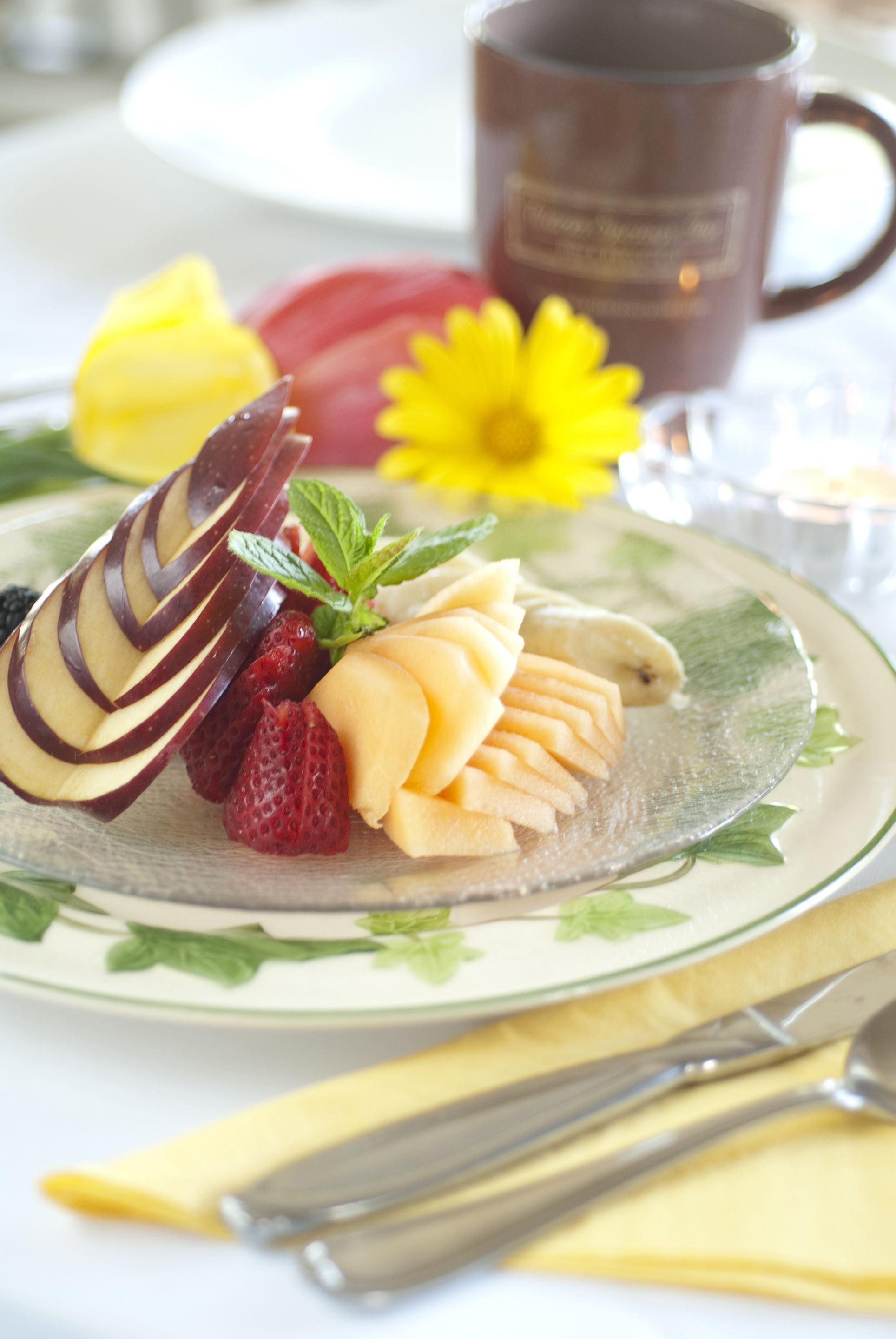 Un plato de frutas cortadas y un postre de chocolate sobre una mesa, con una taza de café al fondo.
