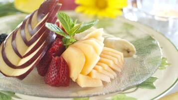 Un plato de frutas cortadas y un postre de chocolate sobre una mesa, con una taza de café al fondo.