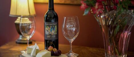 A bottle of Brander Canyon Vineyard Sunny Syrah wine, a glass, and a plate with cheese and grapes on a wooden table.