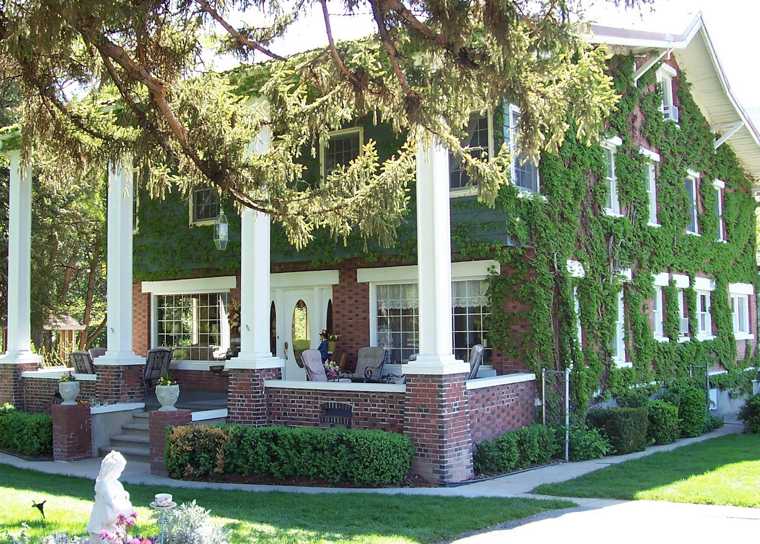A large brick building with a covered porch, columns, and a statue in the front yard.