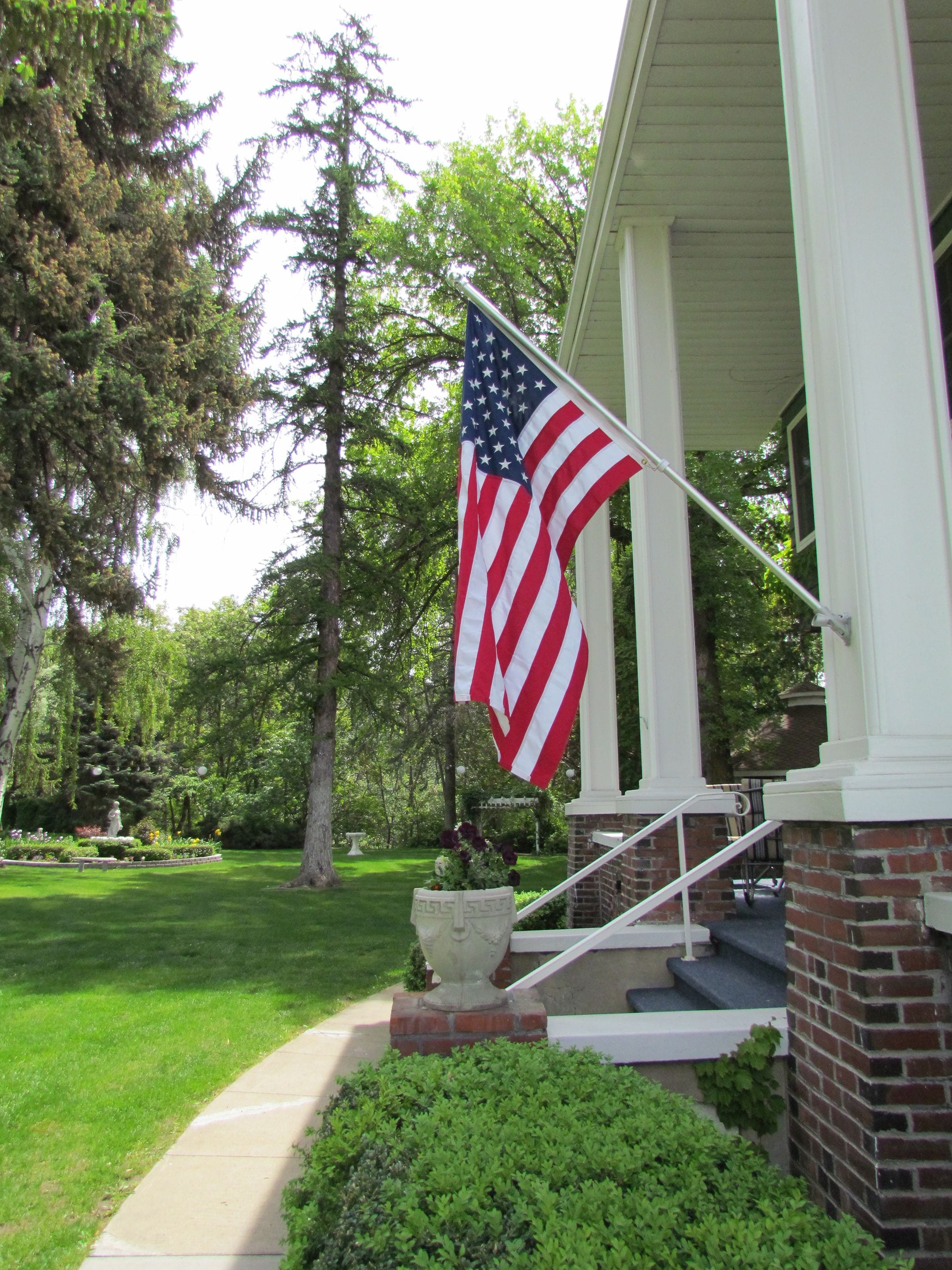 A house with a flagpole displaying an American flag, a brick exterior, and a front porch with steps leading to a door.